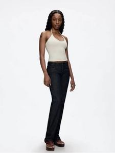Side view of a woman wearing a cream halter top and slim dark blue jeans with sandals
