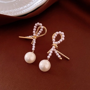 Macro view of gold bow-shaped earrings with delicate pearls on brown velvet