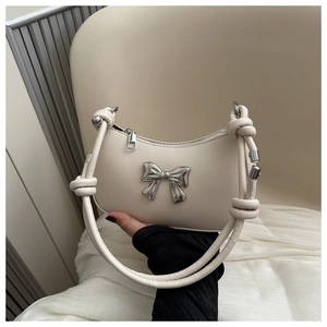 Detail of cream crescent handbag featuring silver metallic bow and knotted shoulder strap