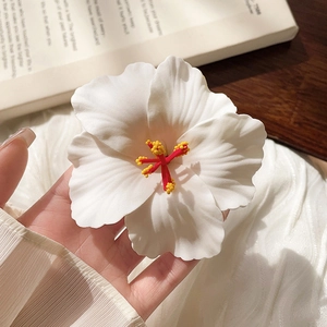 Detailed close-up of a white plumeria flower hair clip with realistic yellow stamen and petals