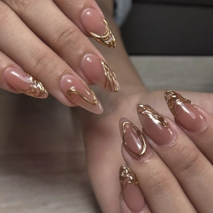 Art 3D fluide doré sur faux ongles amande nude avec une finition métallique brillante