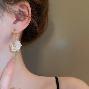 Nahaufnahme goldener Kettchen-Ohrringe mit weißen Perlglanz-Blumen an einem Model
