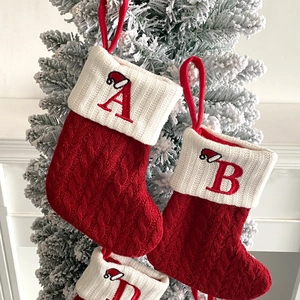 Close-up of red and white knit Christmas stockings with letter embroidery on snowy tree