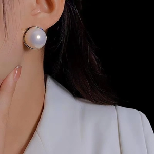 Close-up of a large white pearl stud earring with silver metal frame on a model