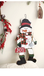 Dettaglio di un pupazzo di neve in legno da parete con scritta JOY e bacche rosse natalizie