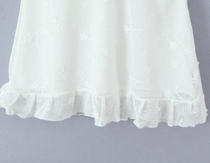 Detail of white mesh lace dress showing floral embroidery and ruffled hemline texture