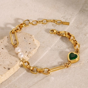 Detailed macro view of gold heart bracelet with green gemstone and white pearls on stone