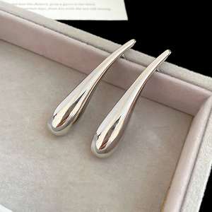 Close-up of long polished silver teardrop earrings on a velvet display tray