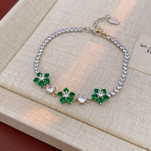 Macro detail of silver flower bracelet with green zircon inlay on textured beige fabric