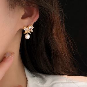 Gros plan de boucles d'oreilles nœud plaquées or avec perles blanches sur le modèle