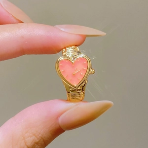 Detail of a gold heart-shaped watch ring with pink dial held between fingers