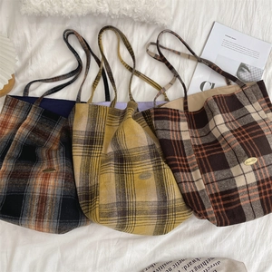 Close-up of three wool plaid tote bags in blue, yellow and brown on a soft white bed