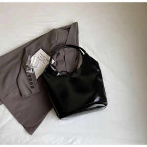 Detailed view of large black glossy leather tote bag on a minimalist urban setting
