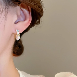Detail of C-shaped enamel earrings with red and blue polka dots on cream background