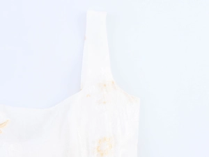 Dettaglio di un abito bianco con spalline larghe e ricami floreali dorati raffinati