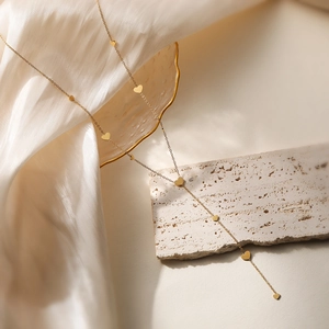 Gold-colored geometric Y-necklace with heart charms on stone and silk background