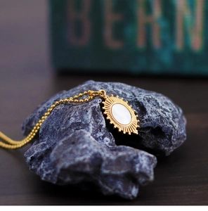 Macro detail of oval shell pendant with sunburst frame on a purple raw stone surface