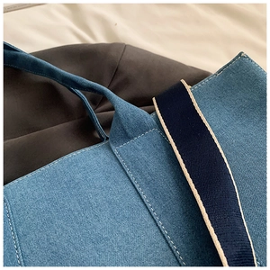 Detailed view of blue denim tote bag with white contrast stitching and durable woven strap