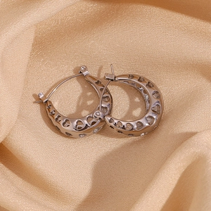 Macro shot of silver hollow heart pattern U-shaped earrings on cream silk fabric
