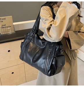 Detail of the black leather tote bag with functional zippers on a model in trench coat