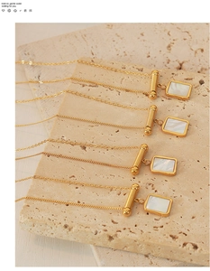 Detail view of gold rectangle pendant with white shell inlay on travertine background