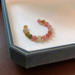 Close-up of geometric beaded ring with colorful gemstones and gold wire on silk lining