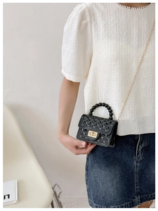 Detail of glossy black quilted PVC bag with beaded handle and gold chain strap