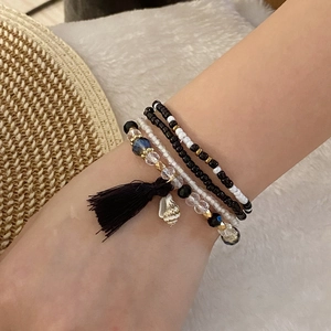 Detail of layered seed bead bracelets with black tassels and seashell charms on wrist