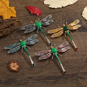 Close-up of assorted dragonfly brooches with faux jade wings on dark wood background