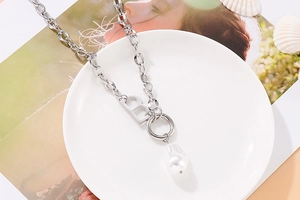 Detailed shot of silver B letter pendant necklace with white baroque pearl on white dish