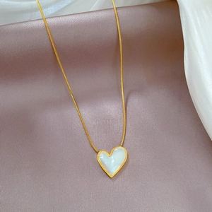 Macro shot of gold snake chain necklace with heart-shaped white mother of pearl pendant
