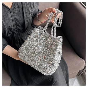 Detail of silver sequin bucket bag with metallic chain strap against dark background