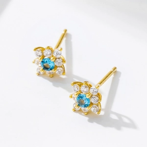 Detail of gold flower stud earring with blue center gemstone and white zircon petals