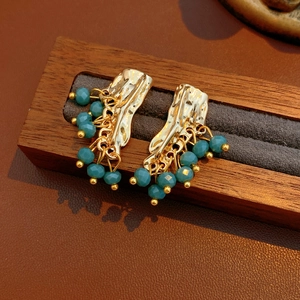 Dettaglio orecchini dorati con texture lava e nappe di perline sfaccettate blu