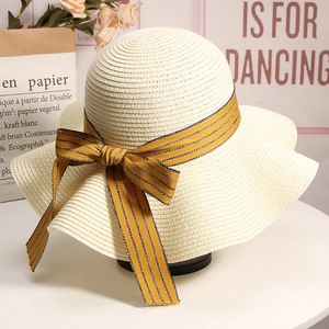 Close-up of beige woven straw sun hat featuring a striped bow and elegant wavy brim