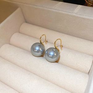 Detailed view of grey pearl earrings with gold hooks inside a beige velvet jewelry box
