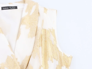 Détail d'une robe élégante sans manches blanche avec jacquard doré et col à revers