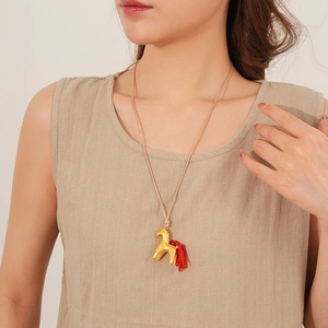 Detail of a golden horse pendant with red tassel on a beige woven wax rope necklace