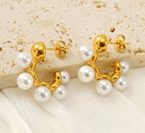 Detail view of C-shaped gold pearl earrings on a premium textured stone background