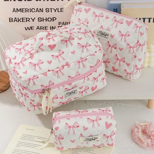 Three pink quilted makeup bags with heart and bow patterns on a cozy aesthetic desk