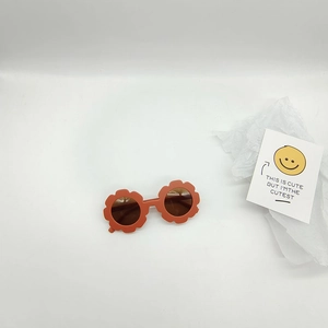 Close-up of orange flower-shaped kids sunglasses on a white background with a smiley card