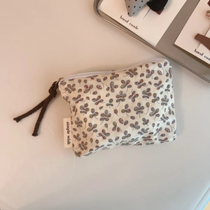 Close-up of linen coin purse with floral pattern, white zipper and simple wish label