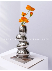 Detail of silver chrome pebble vase with mirror finish and orange poppy flowers on a desk