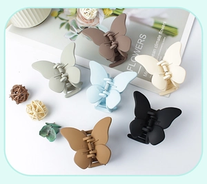Flat lay of six matte butterfly hair clips in earthy tones with floral decorative props