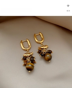 Detailed macro view of 18k gold-plated bird earrings with tiger eye stone and tassels