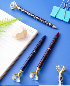 Close-up of metal leopard print pens with large diamond crystal toppers on blue desk