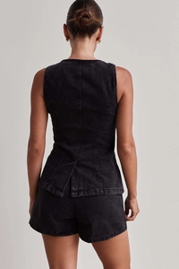 Vista posteriore del gilet in denim nero con spacco e pantaloncini di jeans a vita alta
