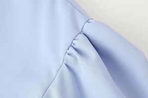 Detail of light blue shirt featuring puff sleeve pleats and smooth woven fabric texture