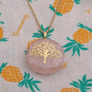 Pink crystal tree of life necklace with a gold chain on a patterned fabric background