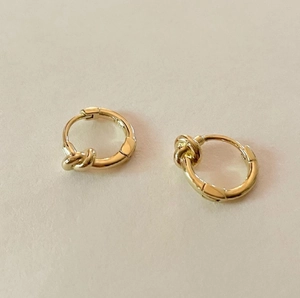 Detail view of golden knot hoop earrings with polished metal texture and hinged closure